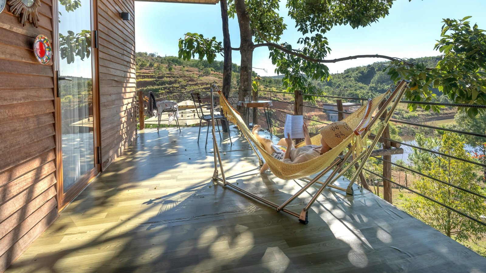 Persona leyendo en la terraza sobre hamaca con soporte, rodeada de naturaleza.