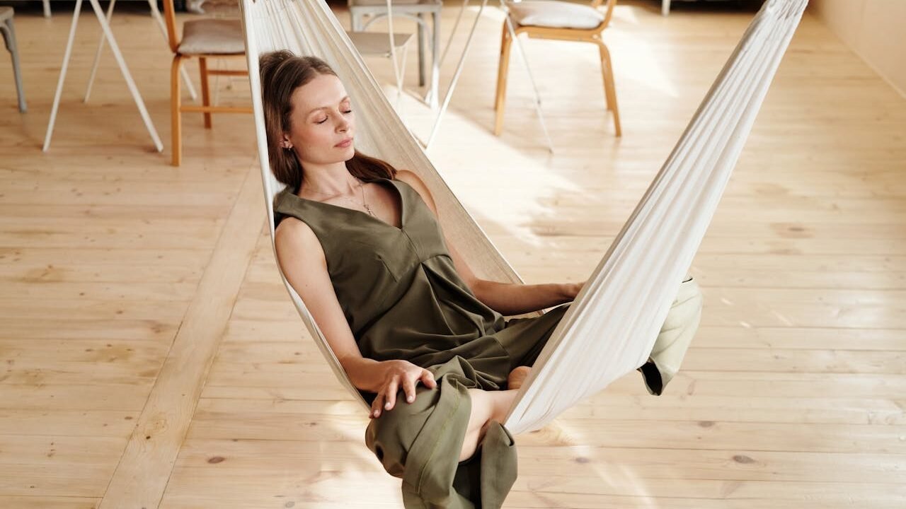 Mujer meditando sobre una hamaca colgable en la sala.