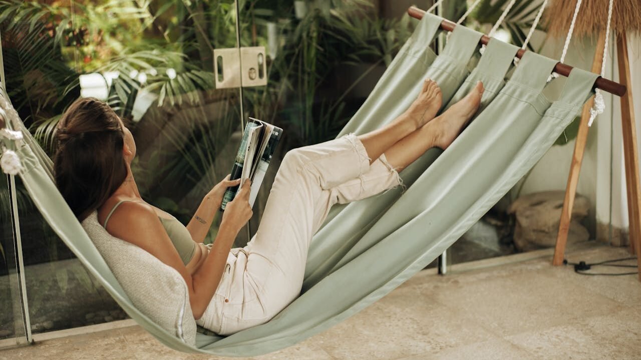 Mujer en hamaca, mirando el exterior con revista en las manos.